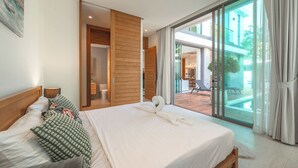 Une chambre d’hôtel moderne dotée d’un grand lit, d’une armoire en bois, d’une porte-fenêtre coulissante donnant sur un balcon, et offrant une vue sur une piscine et un espace de détente extérieur.