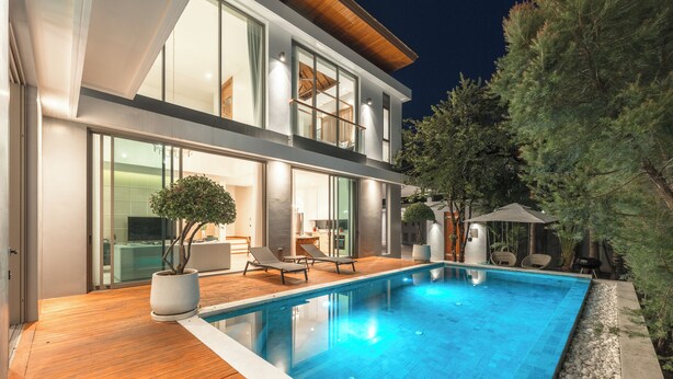 Une maison moderne à deux étages dotée d’une piscine, d’une terrasse en bois et d’un espace salon extérieur.