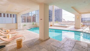 A pool area with lounge chairs, a small pool, and a view of tall buildings.