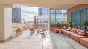 A spacious balcony with a modern sofa, wicker chairs, and potted plants.