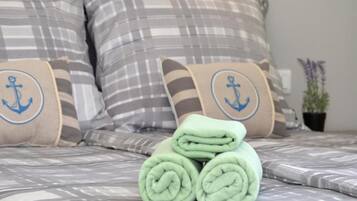 A bed with striped bedding and pillows featuring anchor designs, a neatly rolled green towel, and a potted plant on the side.