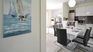 Un espace repas moderne avec une table blanche, des chaises noires et un tableau représentant des voiliers accroché au mur.