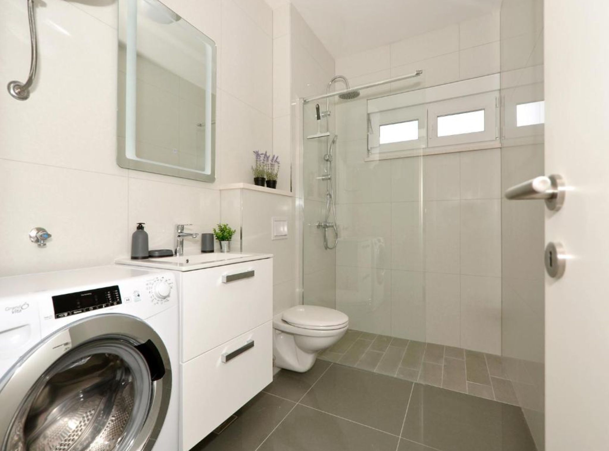 A modern bathroom with a washing machine, toilet, and shower area.
