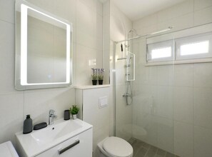 Un baño moderno con lavamanos, espejo y ducha blancos.