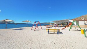 Une plage avec une aire de jeux, des parasols et un bâtiment doté d’un toit rouge.