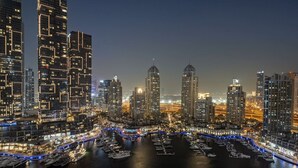 A nighttime cityscape with high-rise buildings and a marina with boats.