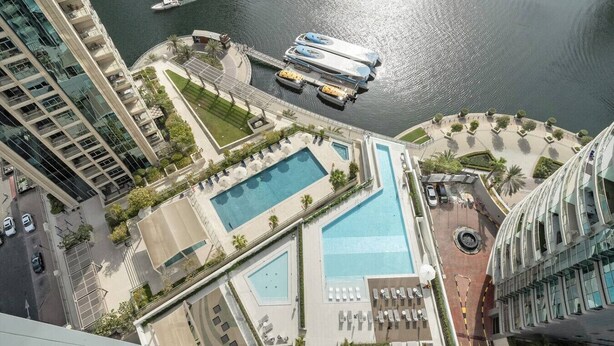 A high-rise hotel with multiple swimming pools, a marina with boats, and a view of the water.