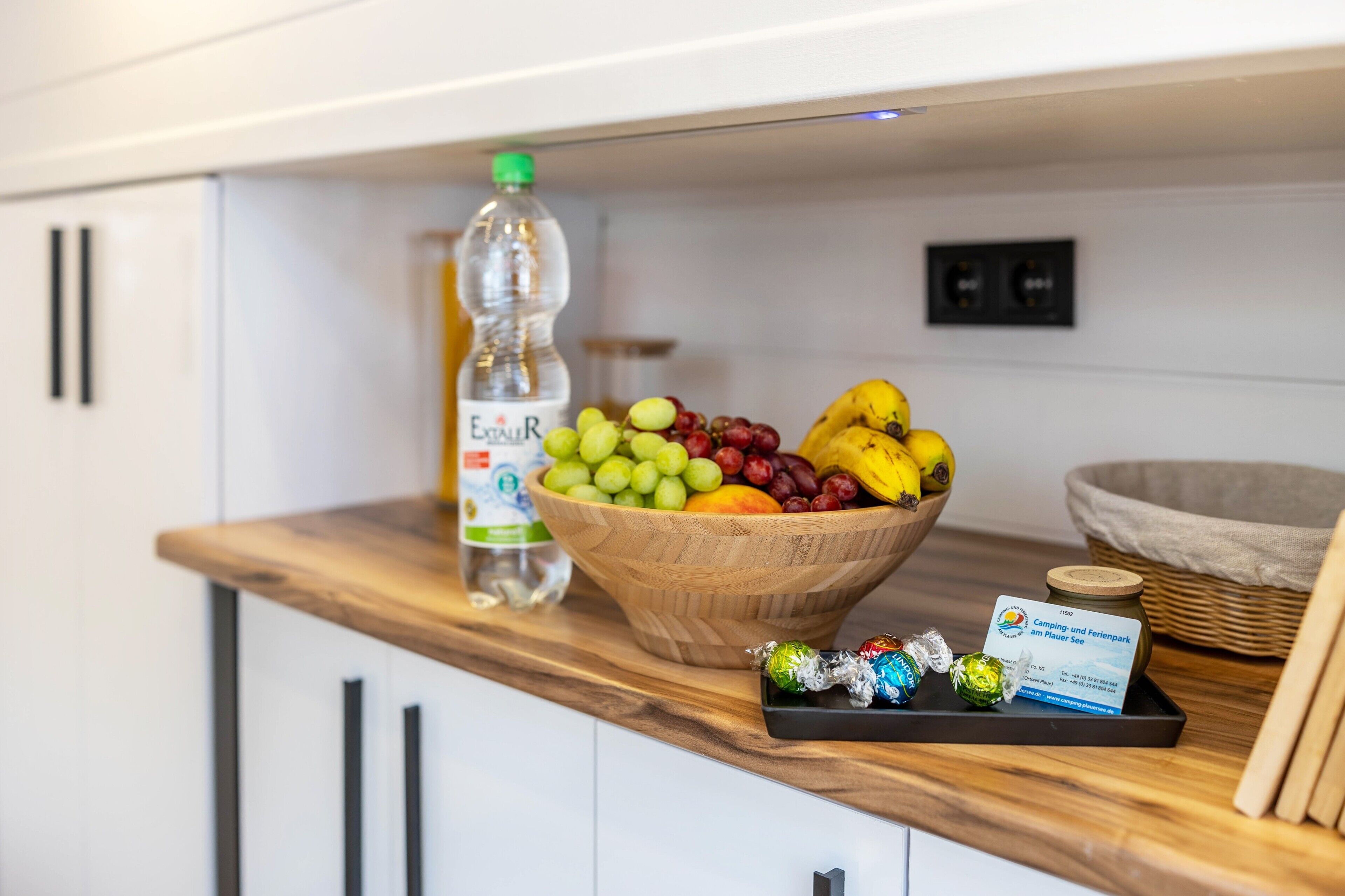 A wooden bowl filled with fruits and a bottle of water on a kitchen counter.