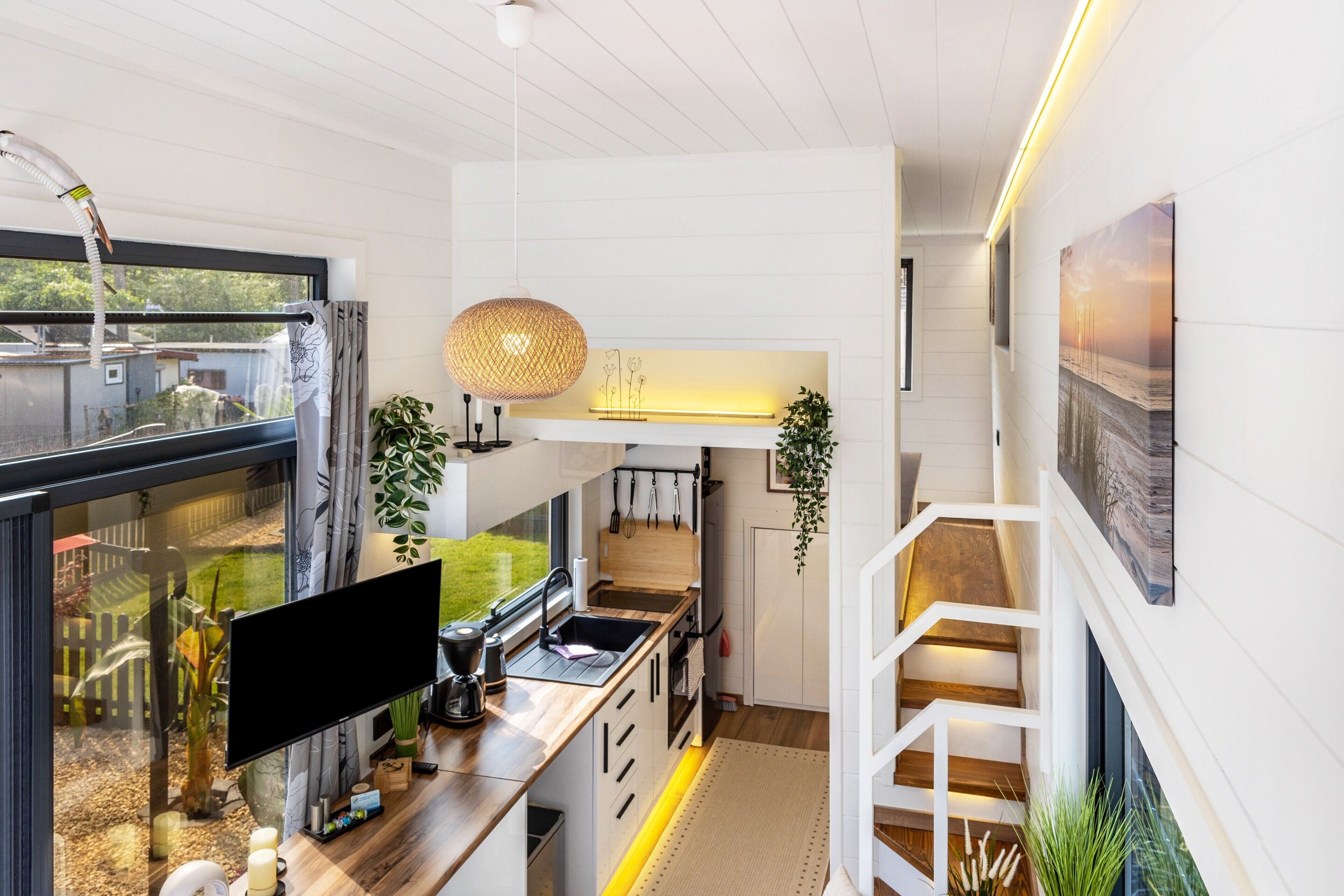 Een moderne keuken met een groot raam, een flatscreen televisie en een houten trap.