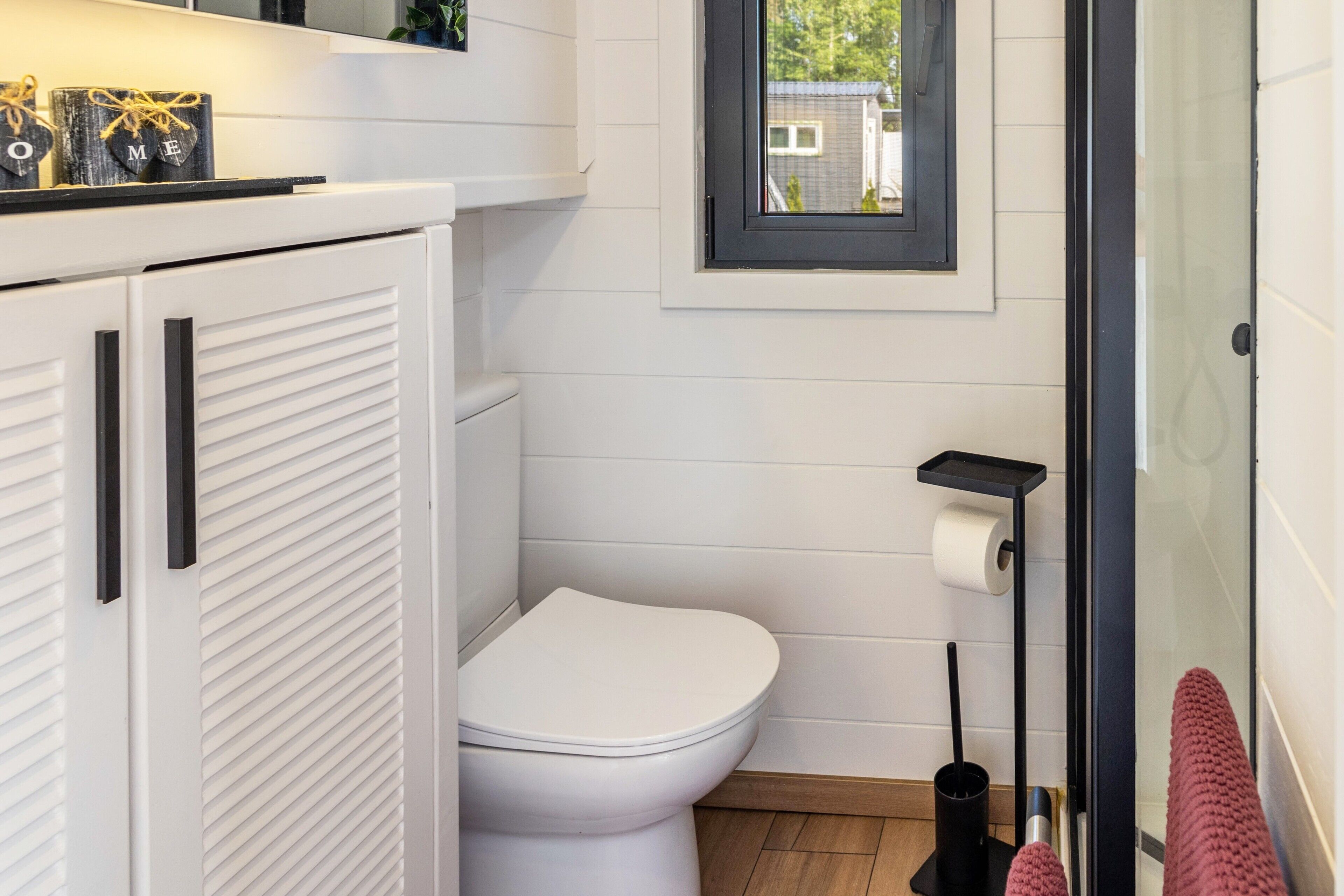Ein Badezimmer mit Toilette, schwarzem Handtuchhalter und einem Fenster mit Blick auf ein Haus.