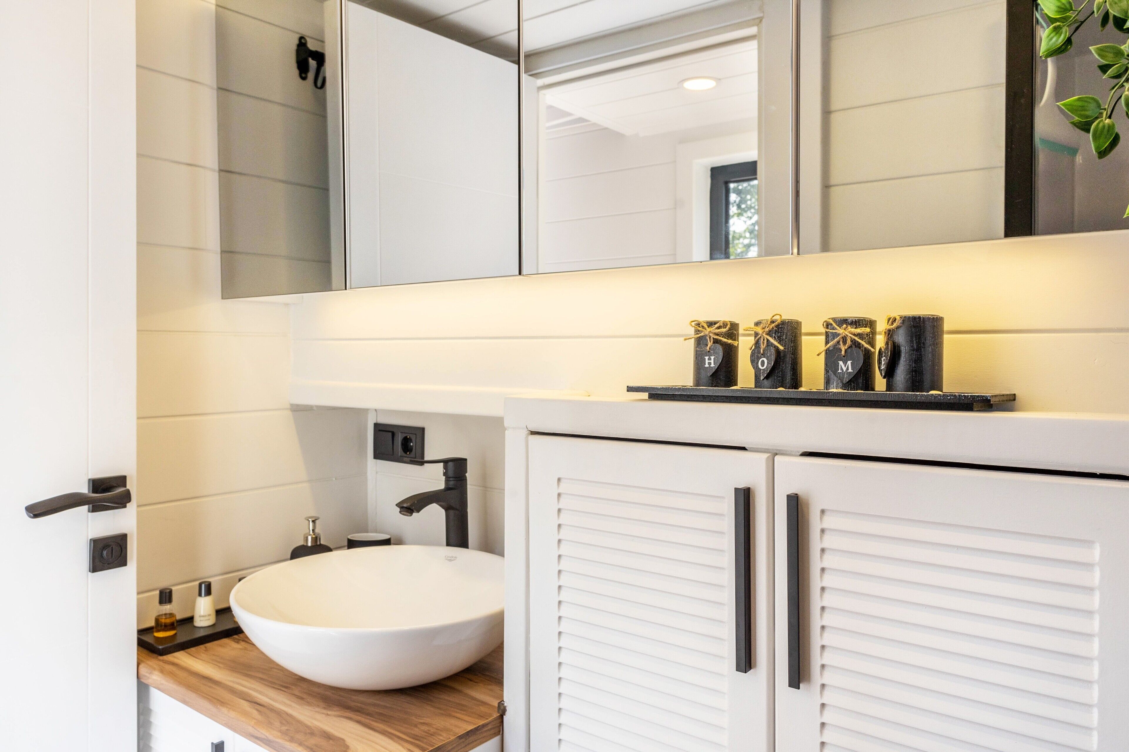 A modern bathroom with a white sink, a mirror, and a cabinet with handles.