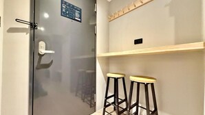 Una habitación con puerta de cristal, dos taburetes de madera y una estantería con lámpara.