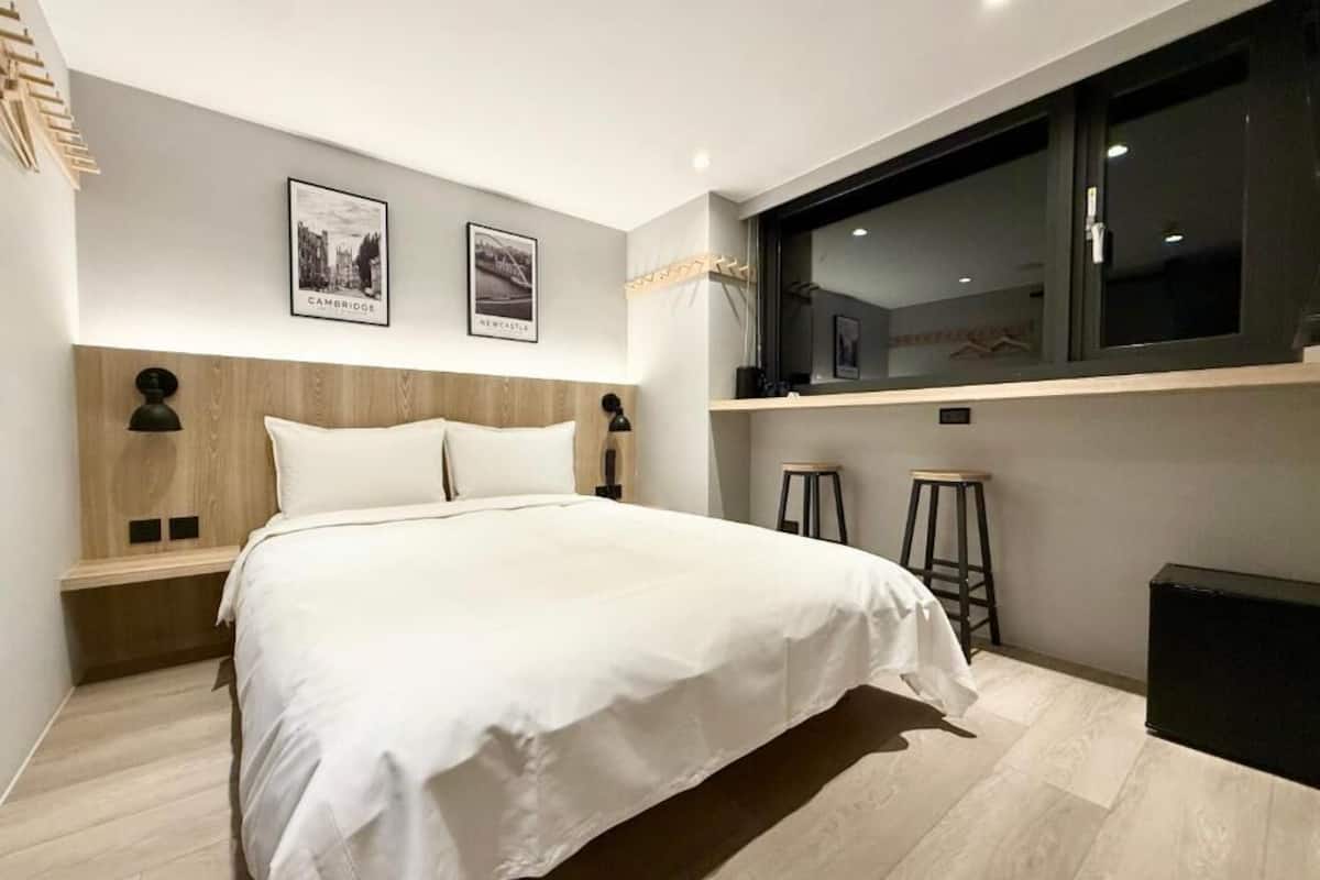 Un dormitorio moderno con una cama grande, dos lámparas fijadas a la pared, una ventana con vistas y dos cuadros enmarcados.
