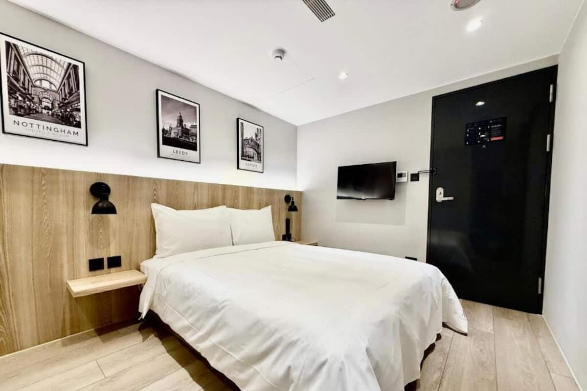 Una habitación de hotel moderna con un cabecero de madera, un televisor de pantalla plana y fotografías enmarcadas de un paisaje urbano.