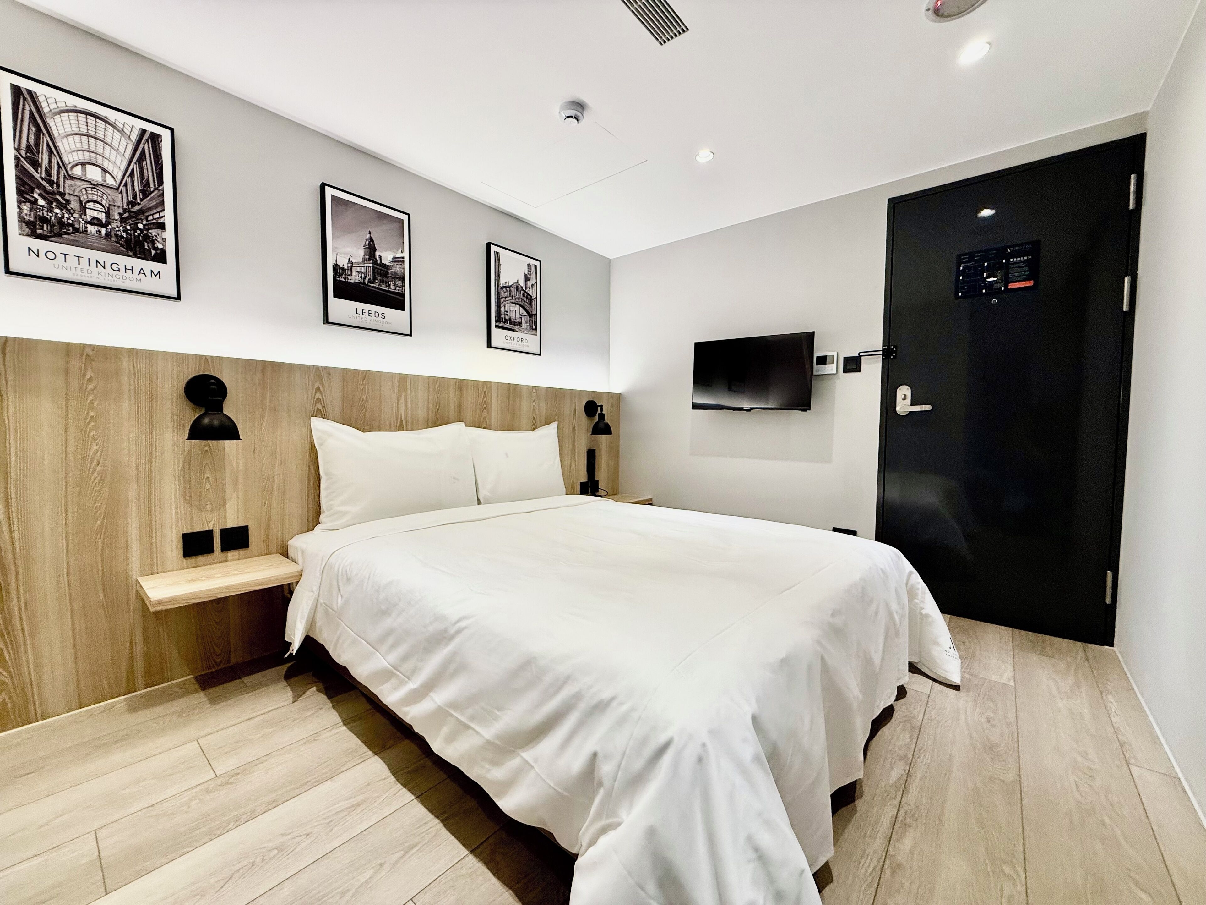 A modern hotel room with a large bed, wooden headboard, and a flat-screen TV mounted on the wall.