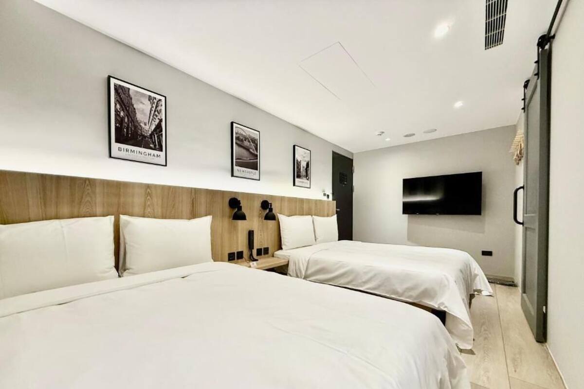 Habitación de hotel con dos camas, cabecera de madera, televisión de pantalla plana y cuadros enmarcados en la pared.