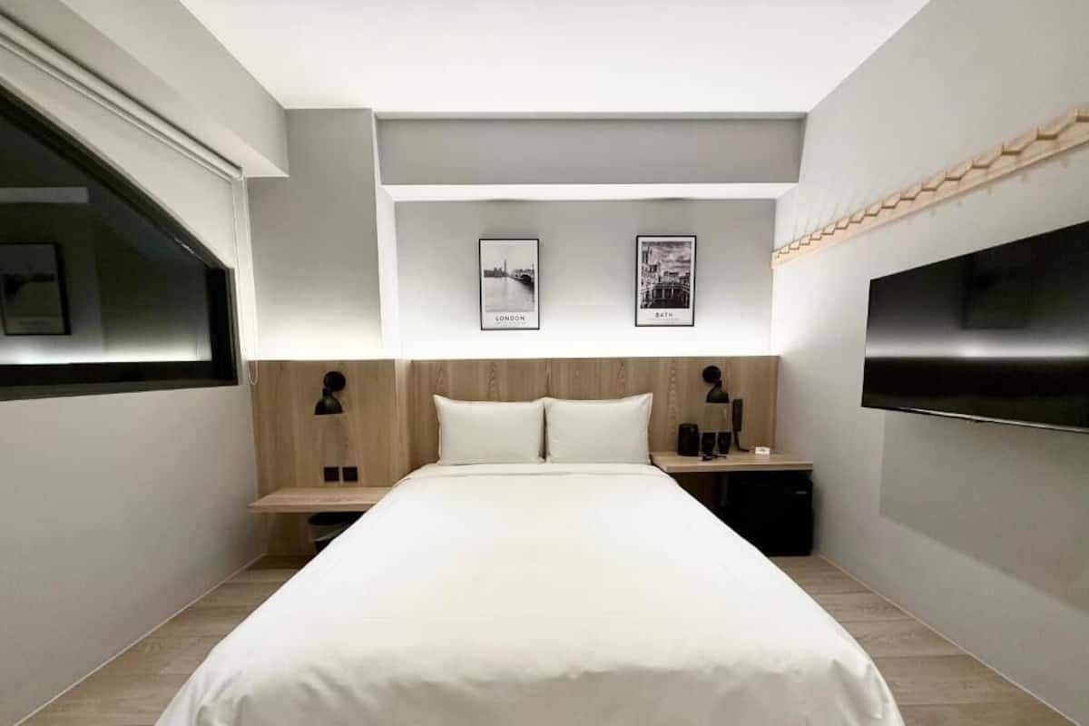 Una habitación de hotel moderna con una cama grande, un televisor de pantalla plana y dos cuadros en la pared.