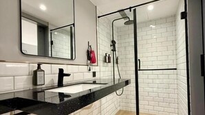 Un baño moderno con encimera negra, azulejos blancos tipo metro y cabina de ducha de vidrio.