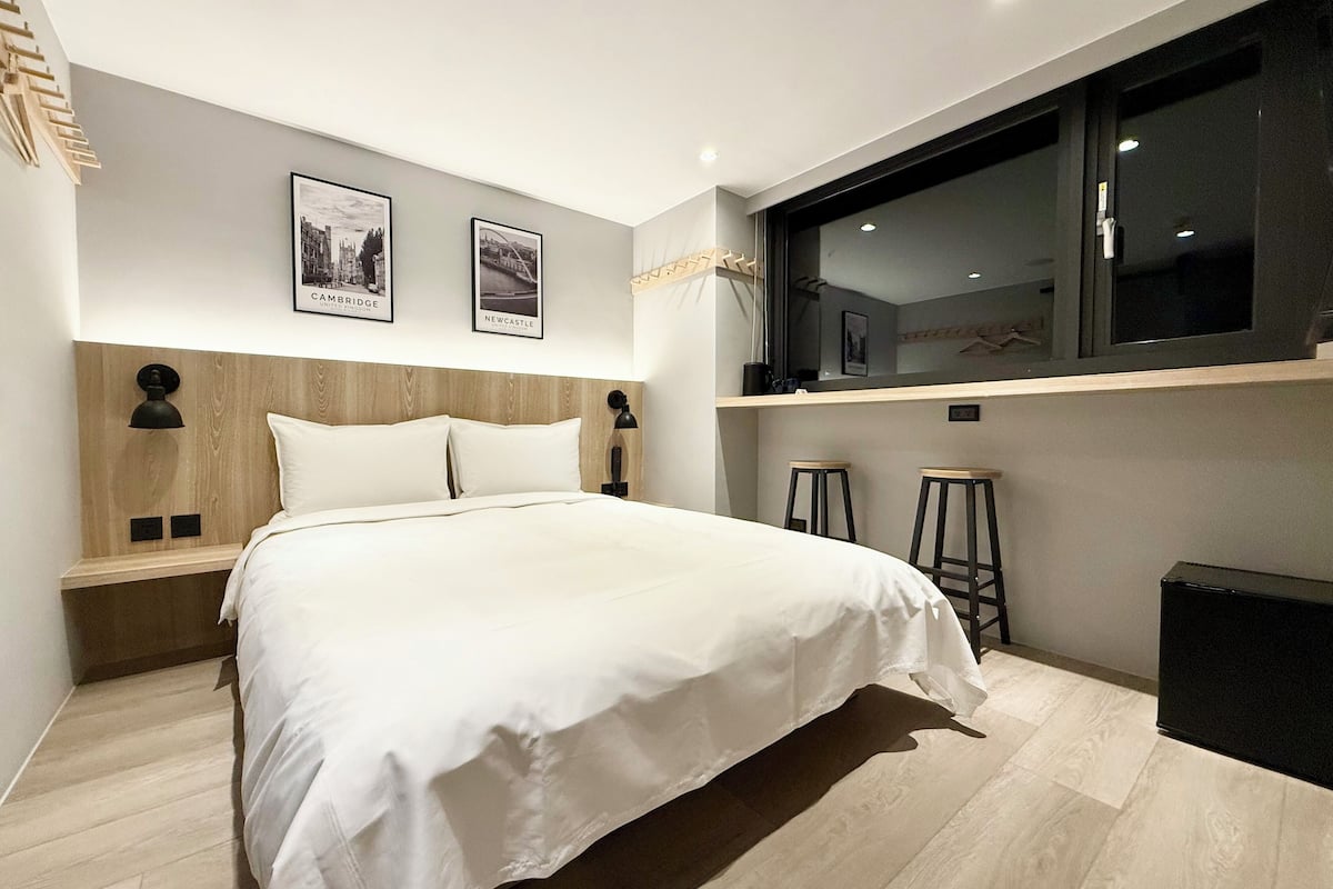 Un dormitorio moderno con una cama grande, dos cuadros en la pared, una ventana y una pequeña zona de bar.