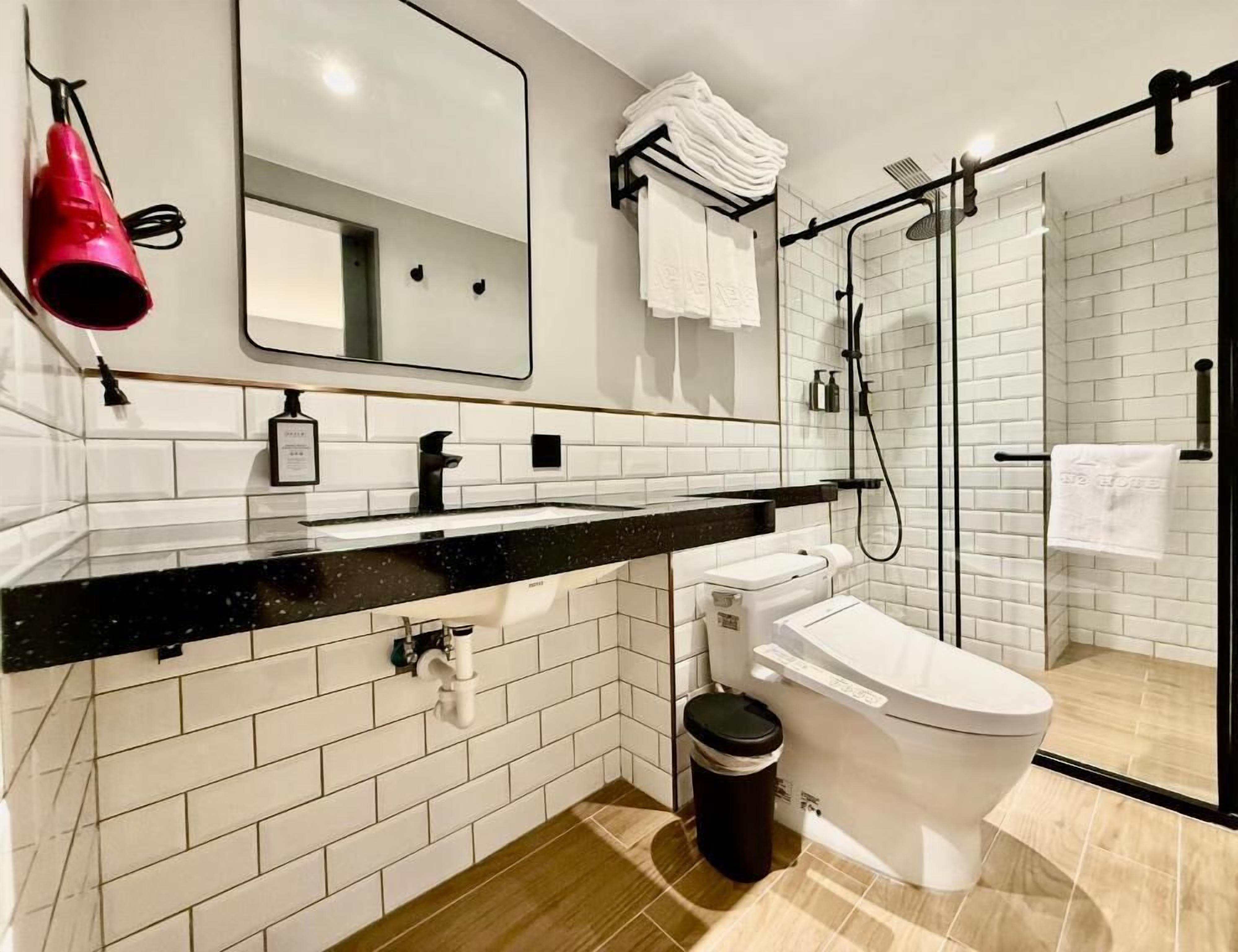 A modern bathroom with a black countertop, white tiles, a glass shower enclosure, and a toilet.