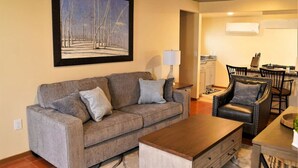 A living room with a grey sofa, a wooden coffee table, a dining area with a table and chairs, and a painting of a snowy path on the wall. - Modern New Mexico Loft in the heart of Las Cruces. (Las Cruces)