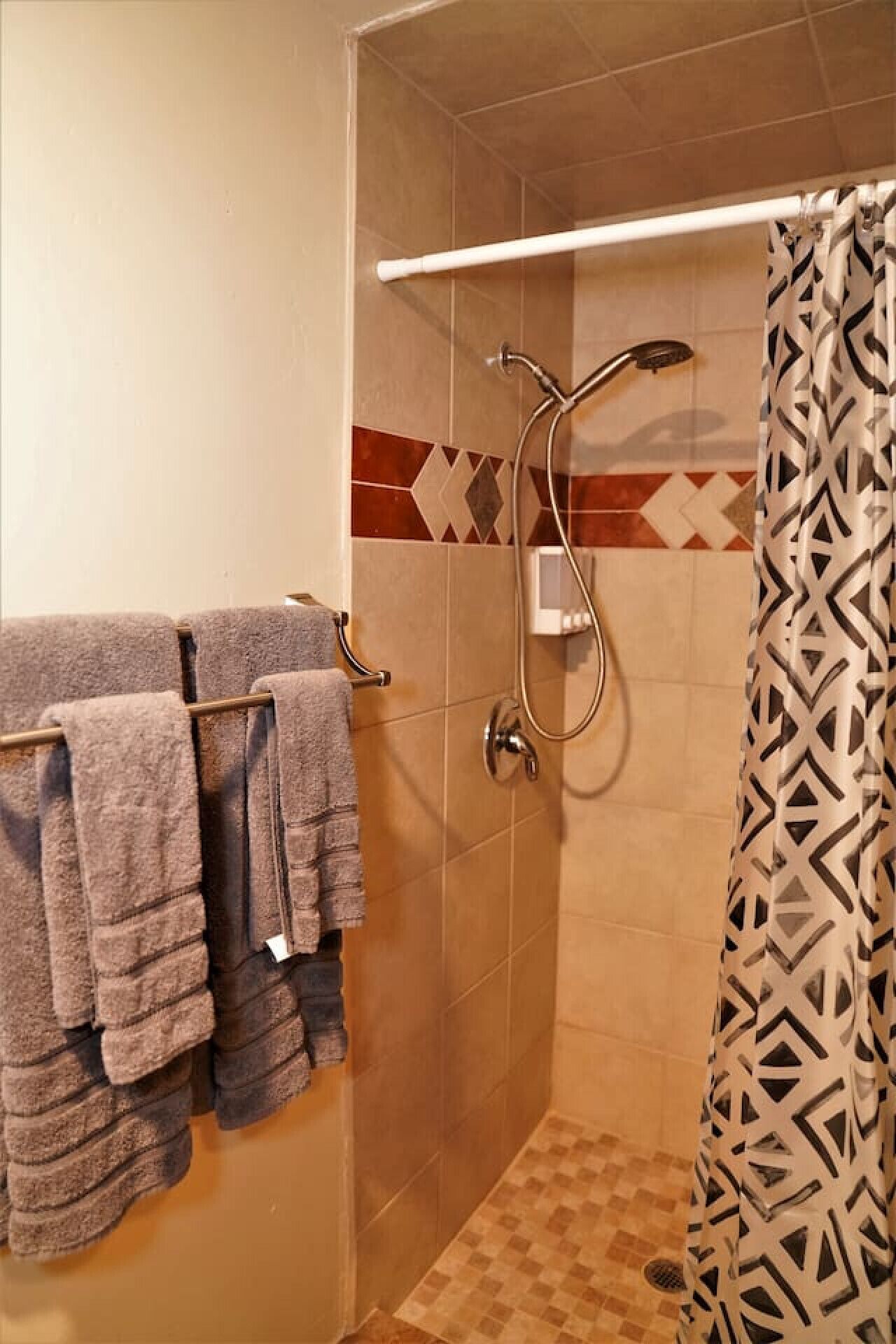 Eine Dusche mit Handbrause, einem Handtuchhalter mit Handtüchern und einem gemusterten Duschvorhang.