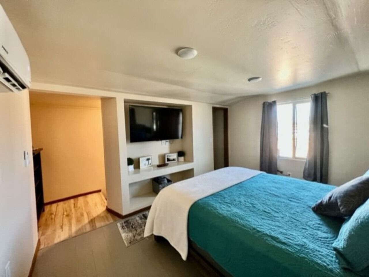 A hotel room with a bed, a TV mounted on the wall, and a window with curtains.