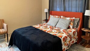 Een slaapkamer met een bed, twee nachtkastjes, een stoel en een plafondventilator.