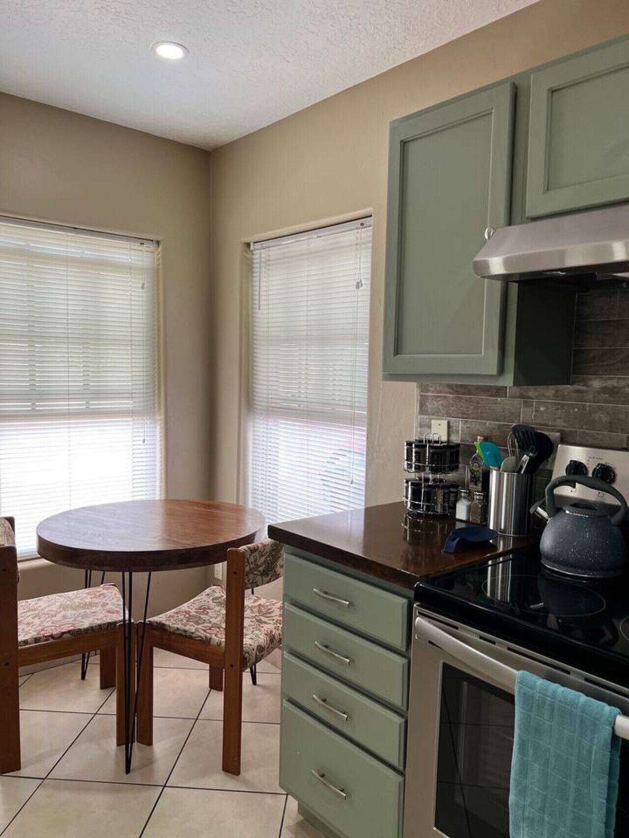 A kitchen with a round table, chairs, a stove, and cabinets.
