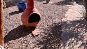 Un espace extérieur rustique agrémenté d’une pergola en bois, d’un grand pot en terre cuite et d’un mur en pierre.
