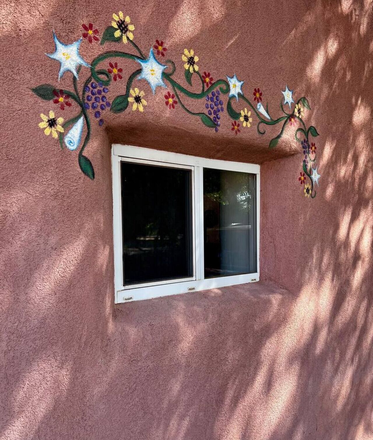 A window with a pink stucco wall and a floral mural above it.