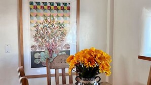 Une table à manger en bois, ornée d’un vase de fleurs, d’une œuvre d’art encadrée et d’un luminaire suspendu au plafond.