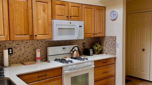 A kitchen with wooden cabinets, a microwave, a stove, and a tiled backsplash. - 2 bd/2bth near NMSU and Memorial Medical Center (Las Cruces)