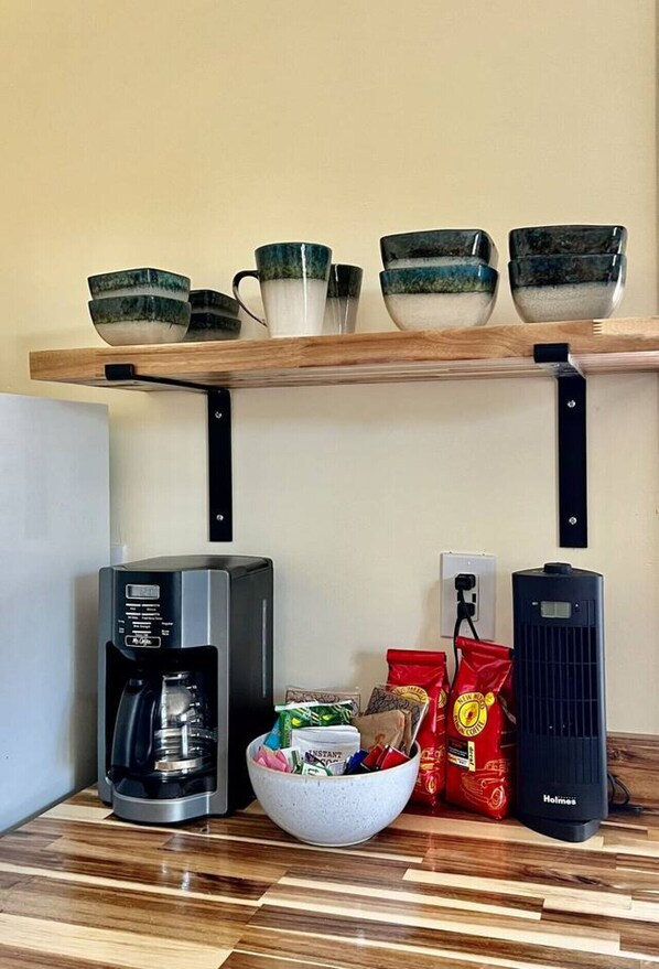 Una zona de cocina con cafetera, un tazón de cápsulas de café y un paquete de granos de café sobre la encimera.