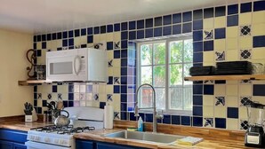 Una cocina con armarios azules, una estufa blanca, un microondas y un ventanal con vistas a zonas verdes.
