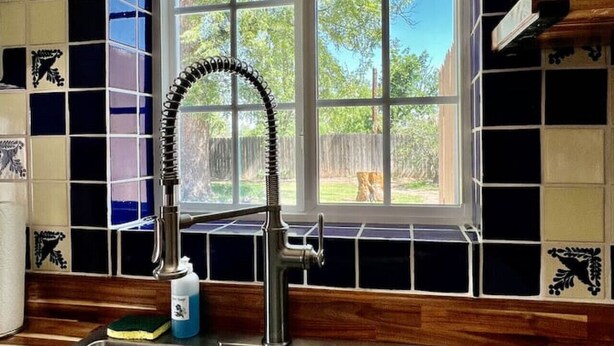 Una cocina con un lavamanos de acero inoxidable, una ventana con vistas a árboles y azulejos decorativos en la pared.