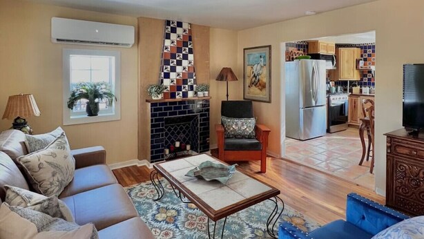 Una sala de estar con sofá, sillón y mesa de centro, una chimenea y una cocina al fondo.