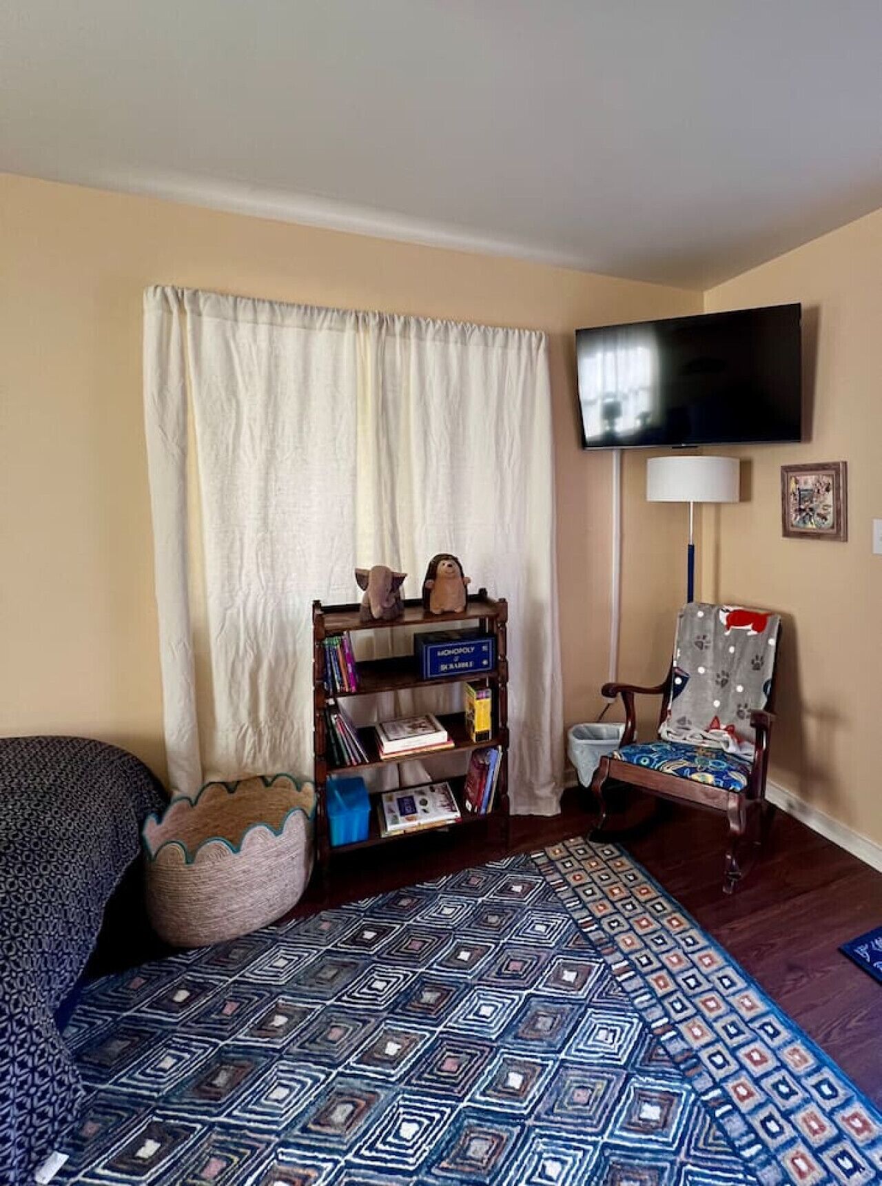 Una sala de estar con un tapete estampado, una estantería, un televisor montado en la pared y un sillón con diseño.