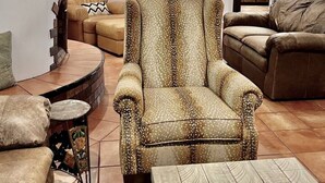 A living room with a patterned armchair, a sofa, and a coffee table. There is a ceiling fan, a fireplace, and a view into the kitchen. - 2 king bds/2.5 bathrooms in the heart of Downtown (Las Cruces)