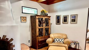 A living room with a fireplace, a leather sofa, a wooden cabinet, and framed pictures on the wall. - 2 king bds/2.5 bathrooms in the heart of Downtown (Las Cruces)