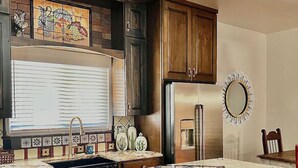 A kitchen with dark wooden cabinets, a stainless steel refrigerator, a tiled backsplash, and a window with blinds. - 2 king bds/2.5 bathrooms in the heart of Downtown (Las Cruces)