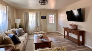 A living room with a sofa, armchair, coffee table, and a TV on the wall. - 1 bed W/D in unit, soaker tub near Field of Dreams (Las Cruces)