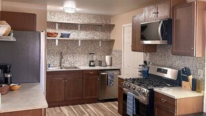 A compact kitchen with wooden cabinets, a built-in microwave, a stove, and a countertop with a blender. - 1 bed W/D in unit, soaker tub near Field of Dreams (Las Cruces)