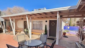 A covered patio with a round table and chairs, a barbecue grill, and a view of a mountain landscape.