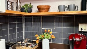 A kitchen with a toaster, coffee maker, and a vase with tulips. There are shelves with decorative items and a tiled backsplash.