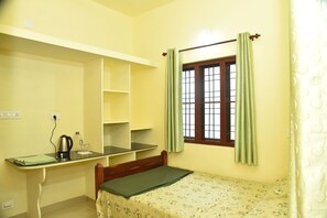 Una habitación pequeña y luminosa con una cama individual, un escritorio con una silla y una ventana con cortinas.