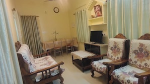 A living room with a dining table, chairs, a television, and a small shrine.