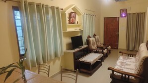 A living room with a TV, wooden furniture, and a shelf with decorative items.