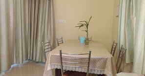 Un comedor con una mesa cubierta por un mantel de encaje, rodeada de sillas de metal. Hay una planta en maceta sobre la mesa.