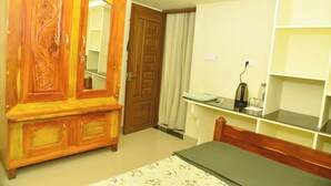 A bedroom with a wooden wardrobe, a bed, a nightstand, and a shelf with a kettle.